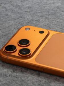 Orange smartphone with dual cameras placed on a soft gray fabric surface.