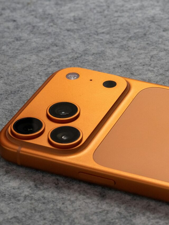 Orange smartphone with dual cameras placed on a soft gray fabric surface.