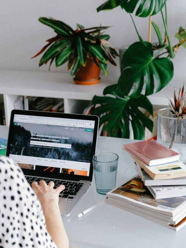 A woman working from home on her laptop surrounded by plants and books for a cozy office feel.