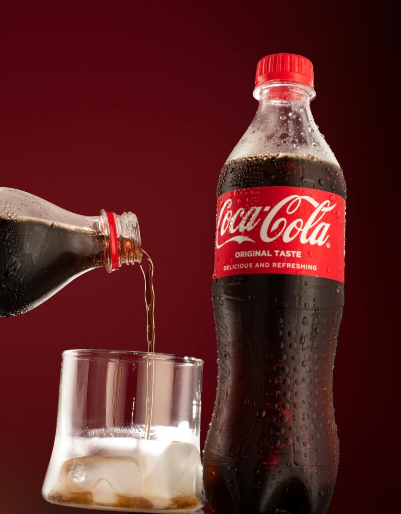 Coca-Cola being poured into a glass with ice cubes against a red background.